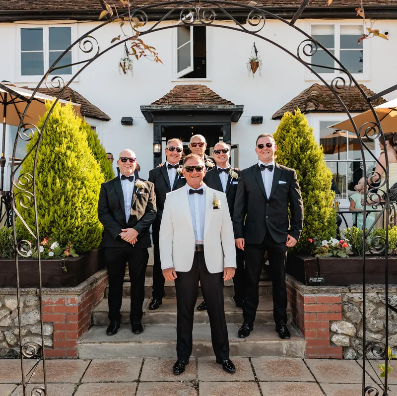 Groom and groomsmen under a garden arch at The Orchard