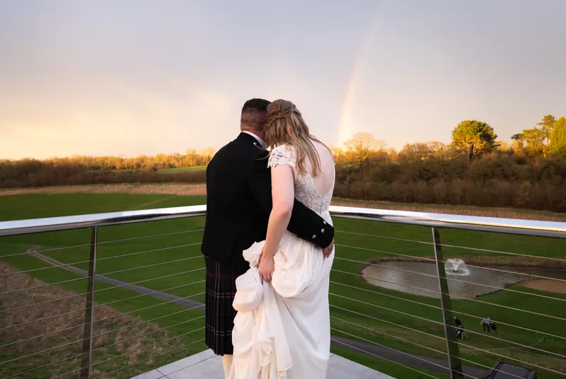 Couple watching a rainbow over the fields from a balcony