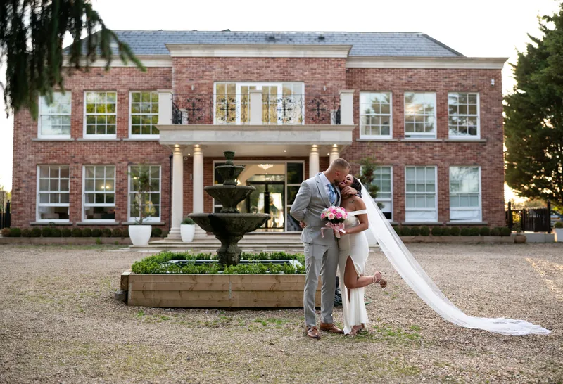 Couple kissing by the fountain in front of a country house wedding venue in Kent