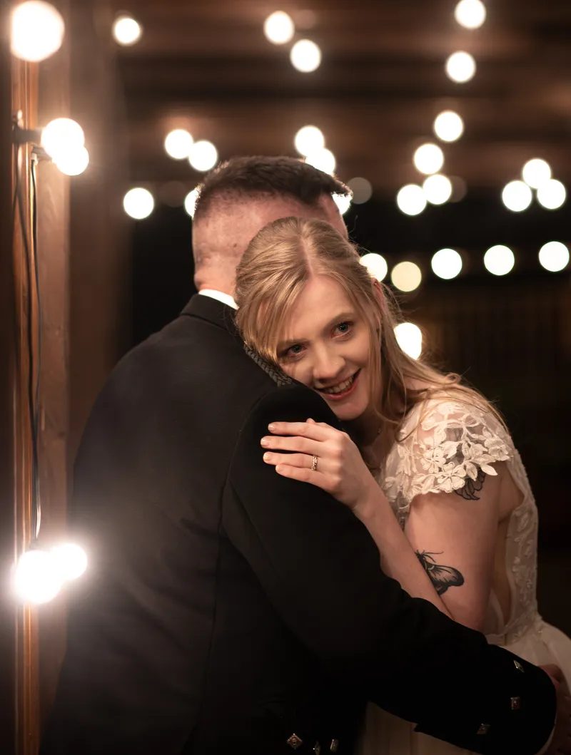 Bride hugging the groom under festoon lights