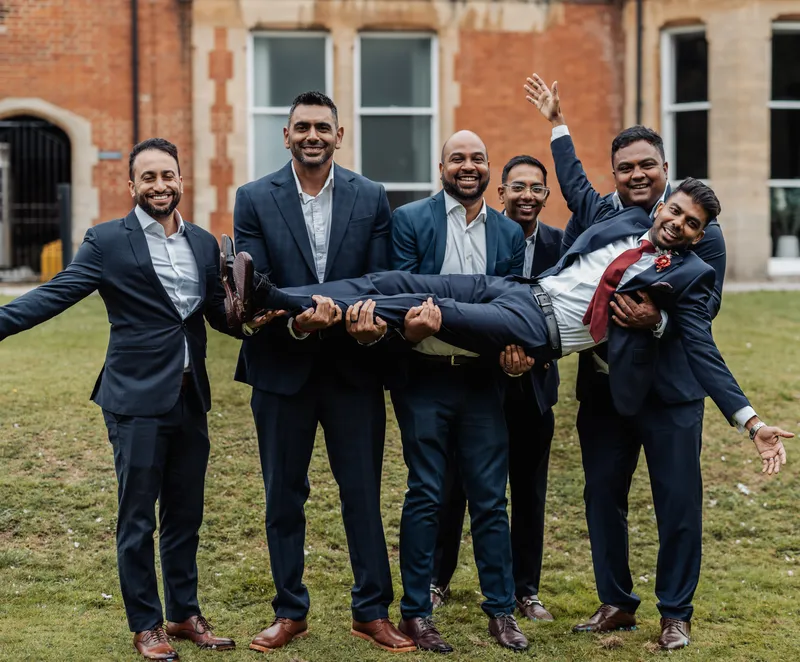 Groomsmen lifting a friend on the lawn at Oakwood House