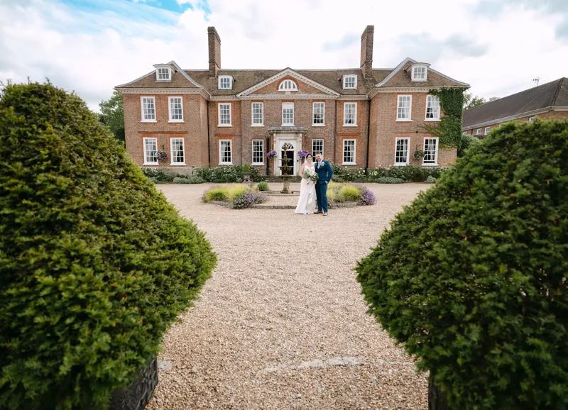 Couple on the gravel forecourt framed by topiary at Chilston Park
