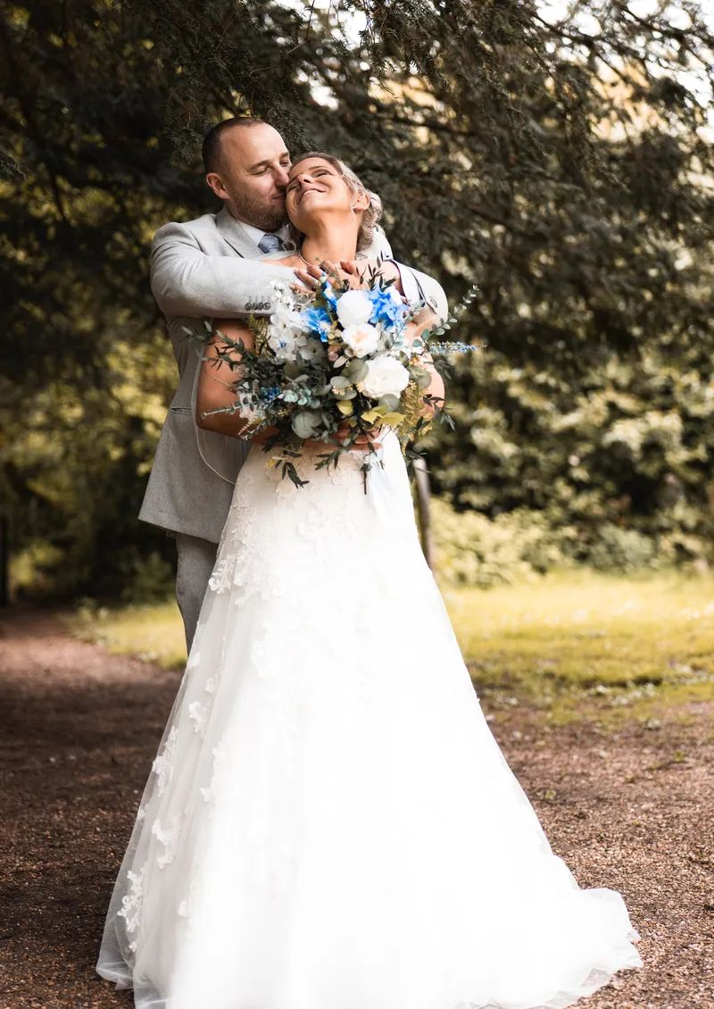 Groom hugging the bride as she laughs, bouquet in hand