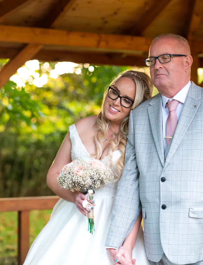 Bride and her father smiling under a wooden shelter