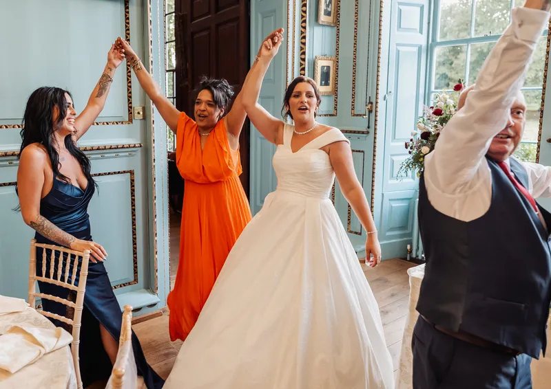 Bride and friends dancing with arms raised at Bradbourne House