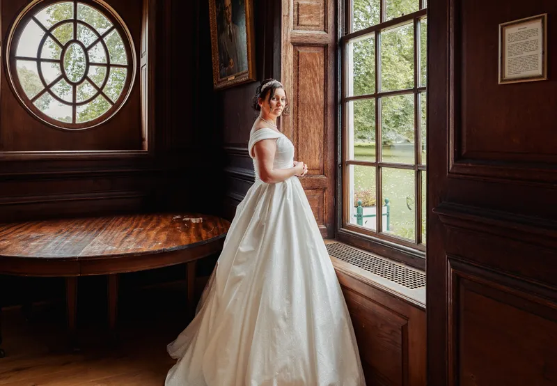 Bride by the window in the oak-panelled room with round windows at Bradbourne House