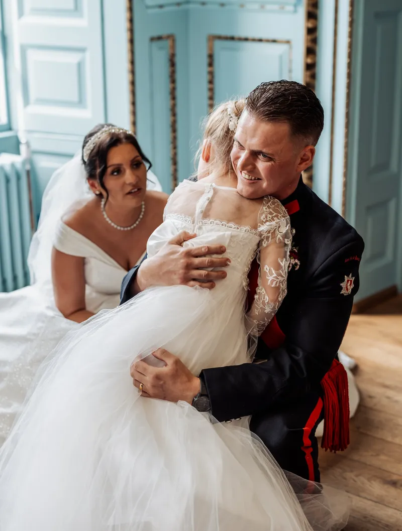 Groom hugging the flower girl as the bride looks on at Bradbourne House