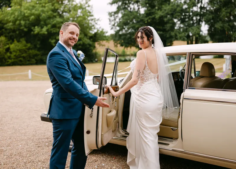 Groom holding the door of the classic wedding car for the bride at Chilston Park Hotel