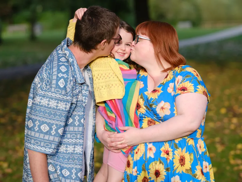 Parents kissing their smiling daughter's cheeks at Cobtree Manor Park, Maidstone