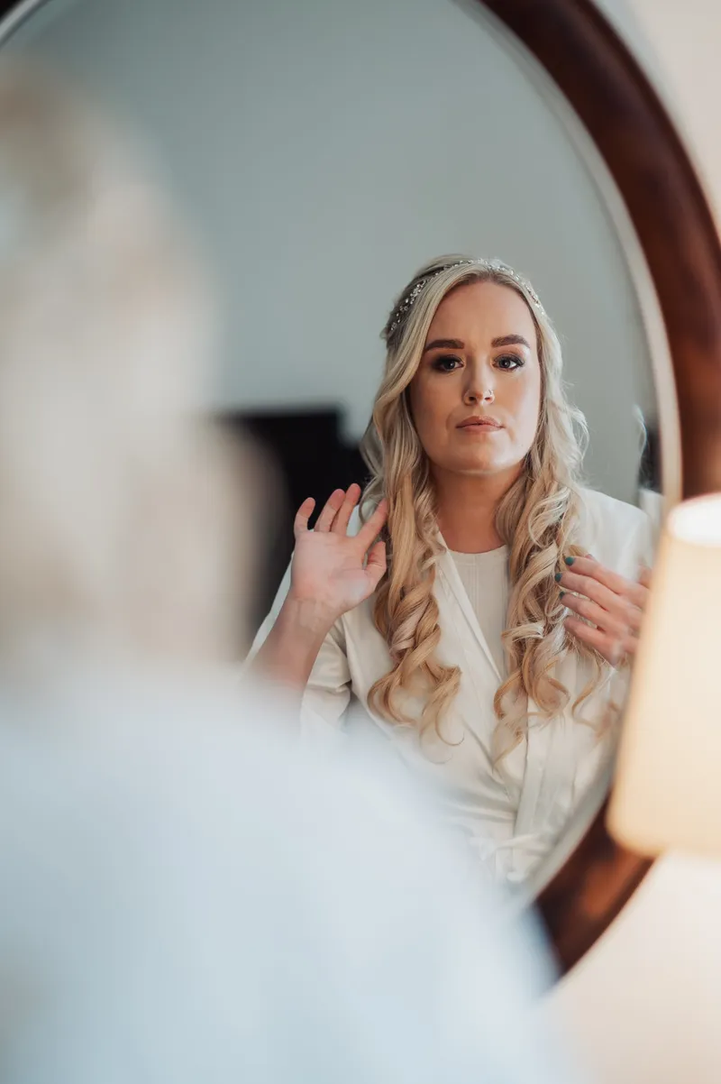 Bride looking thoughtfully at her reflection in an oval mirror while getting ready