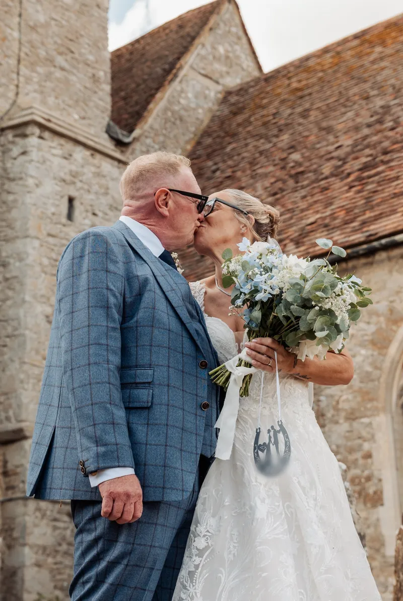 Bride and groom kissing outside a medieval stone church in Kent
