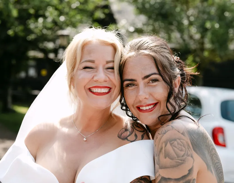 Bride and her friend smiling cheek to cheek on the wedding day