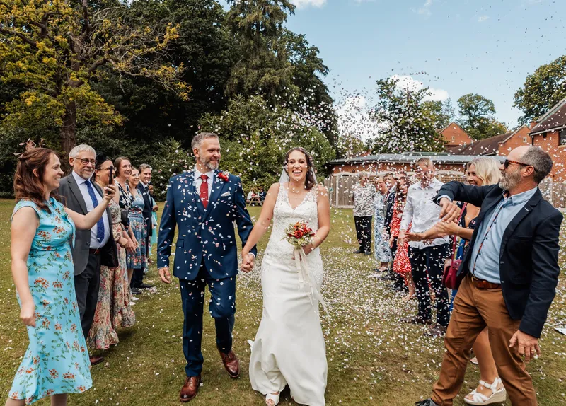Bride and groom laughing as guests throw confetti on the lawn at a Kent wedding