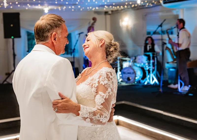 Bride smiling up at the groom during their first dance with the live band playing behind