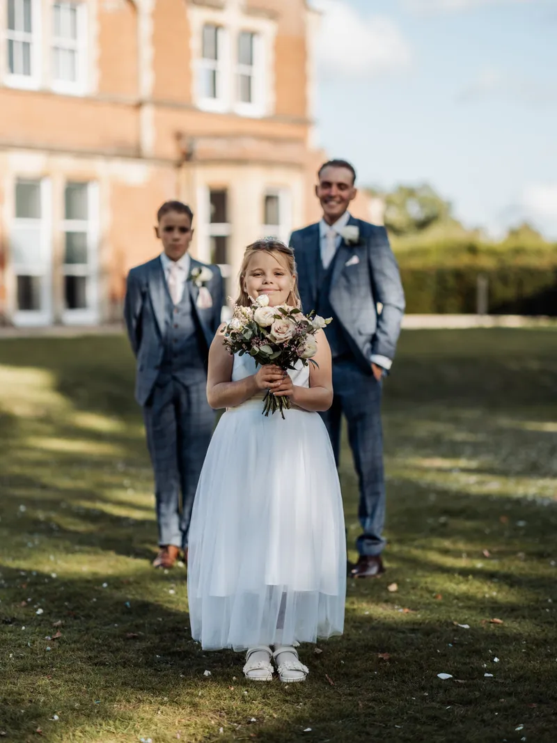 Flower girl holding the bouquet with page boys behind her on the lawn