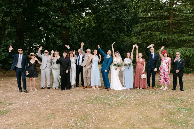 Bride, groom and their families waving and cheering for the group photo on the lawn