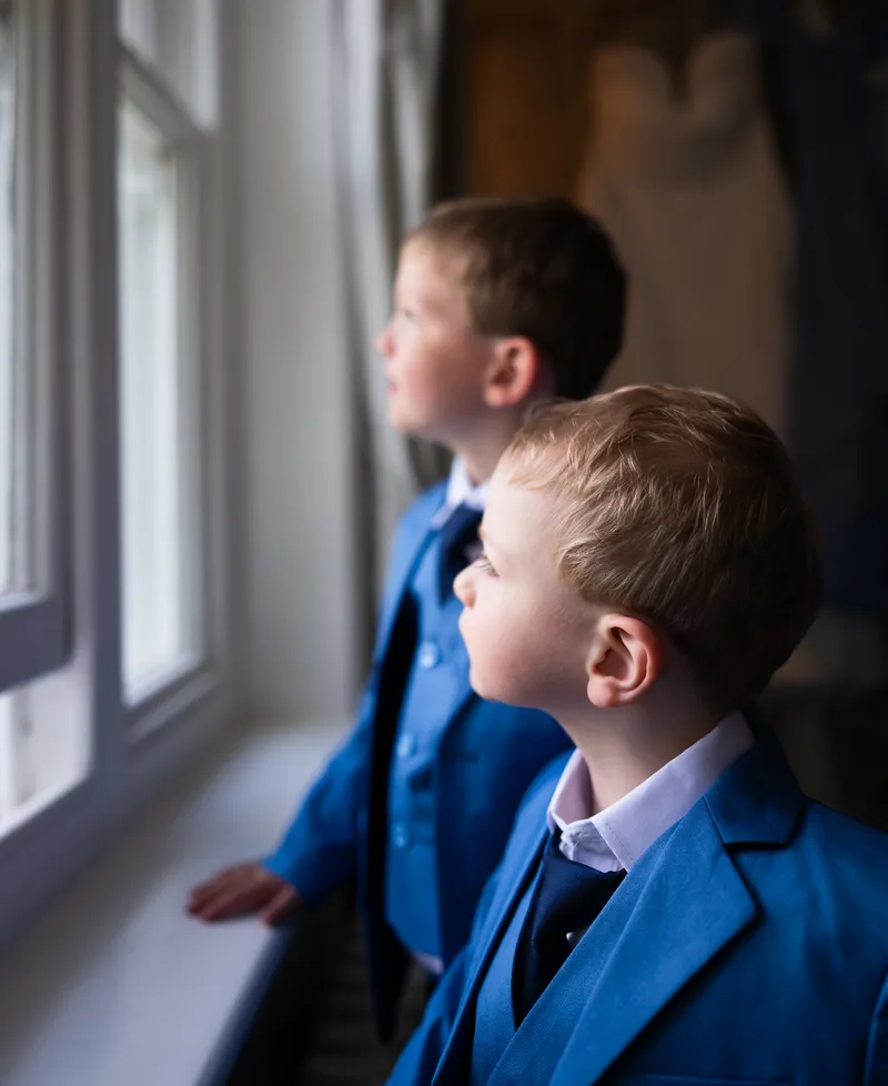 Two page boys in blue suits looking out of the window