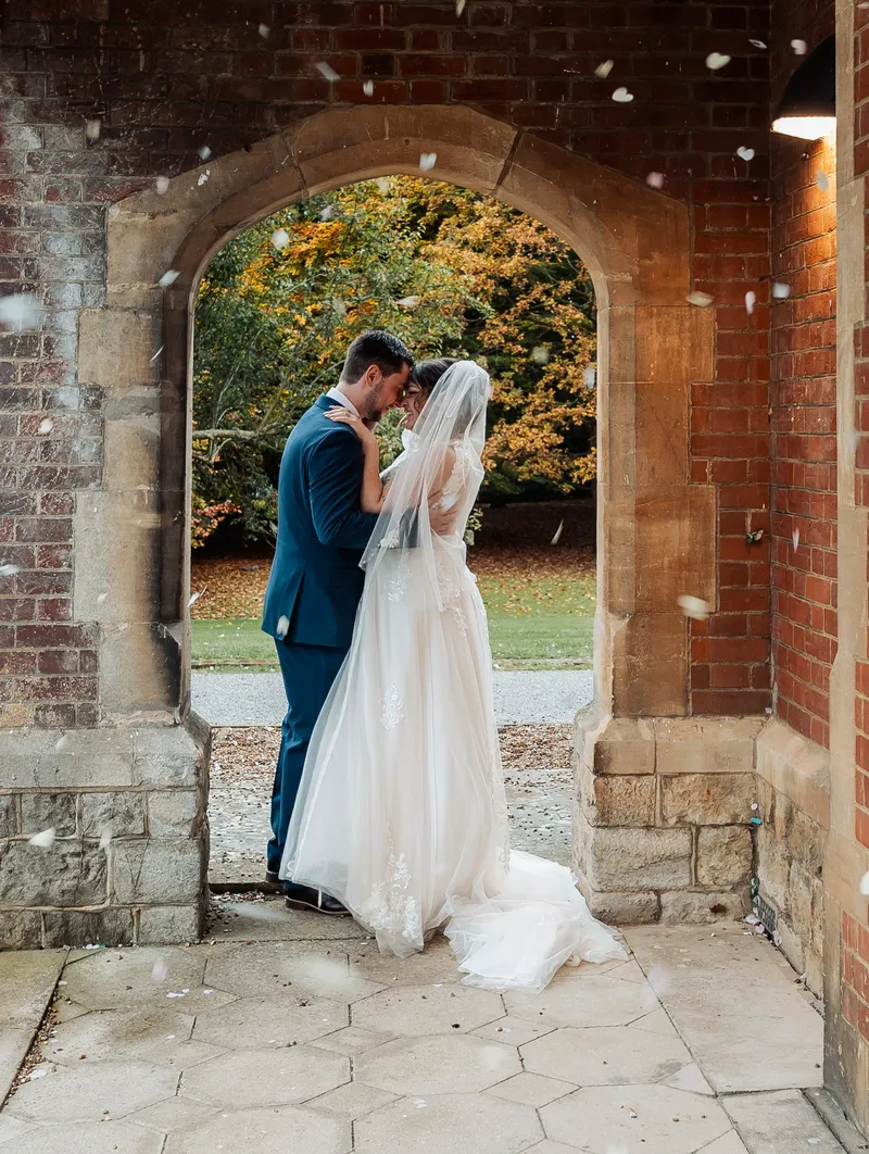 Confetti falling around the couple in the brick arch at Oakwood House in autumn