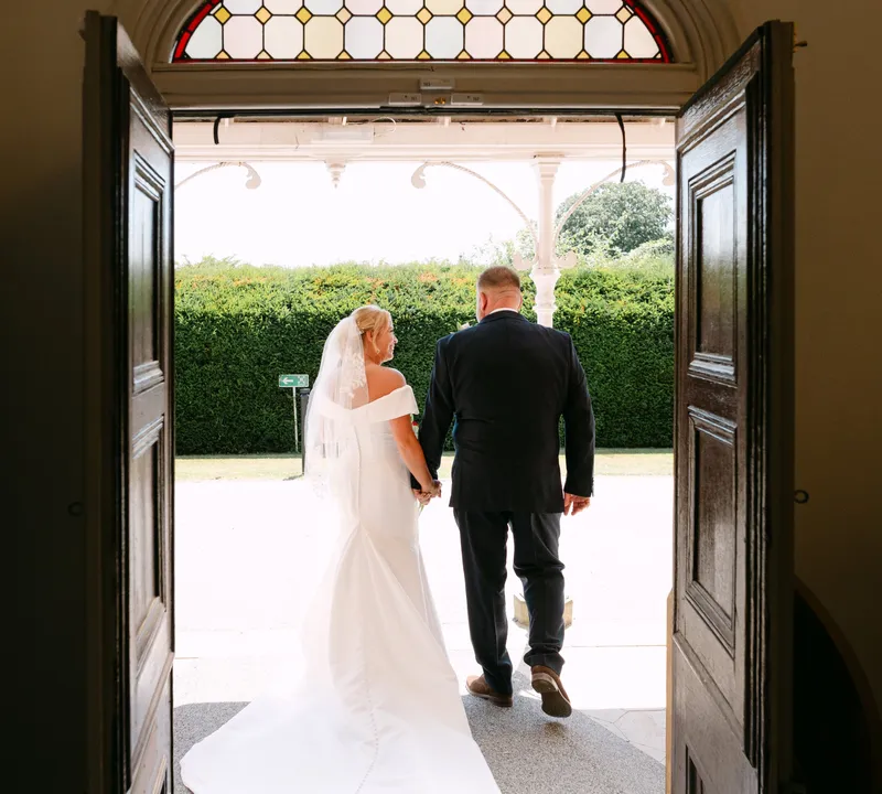 Bride and groom walking out through the doors under the stained glass at Oakwood House