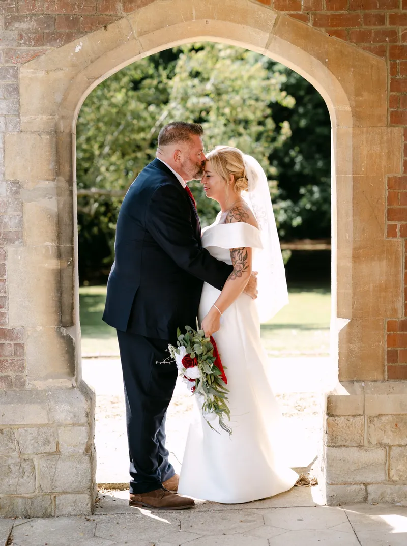 Groom kissing the bride's forehead in the brick arch at Oakwood House, Maidstone