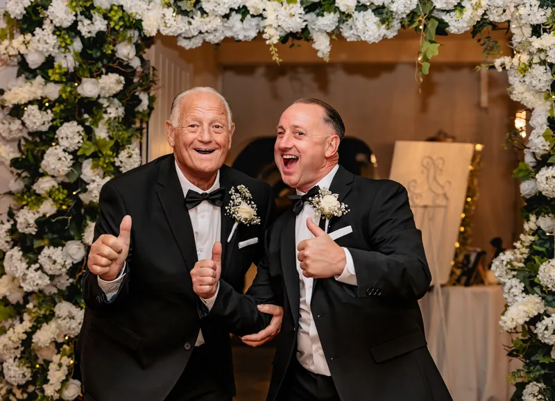 Two guests giving a thumbs up under the flower arch at The Orchard